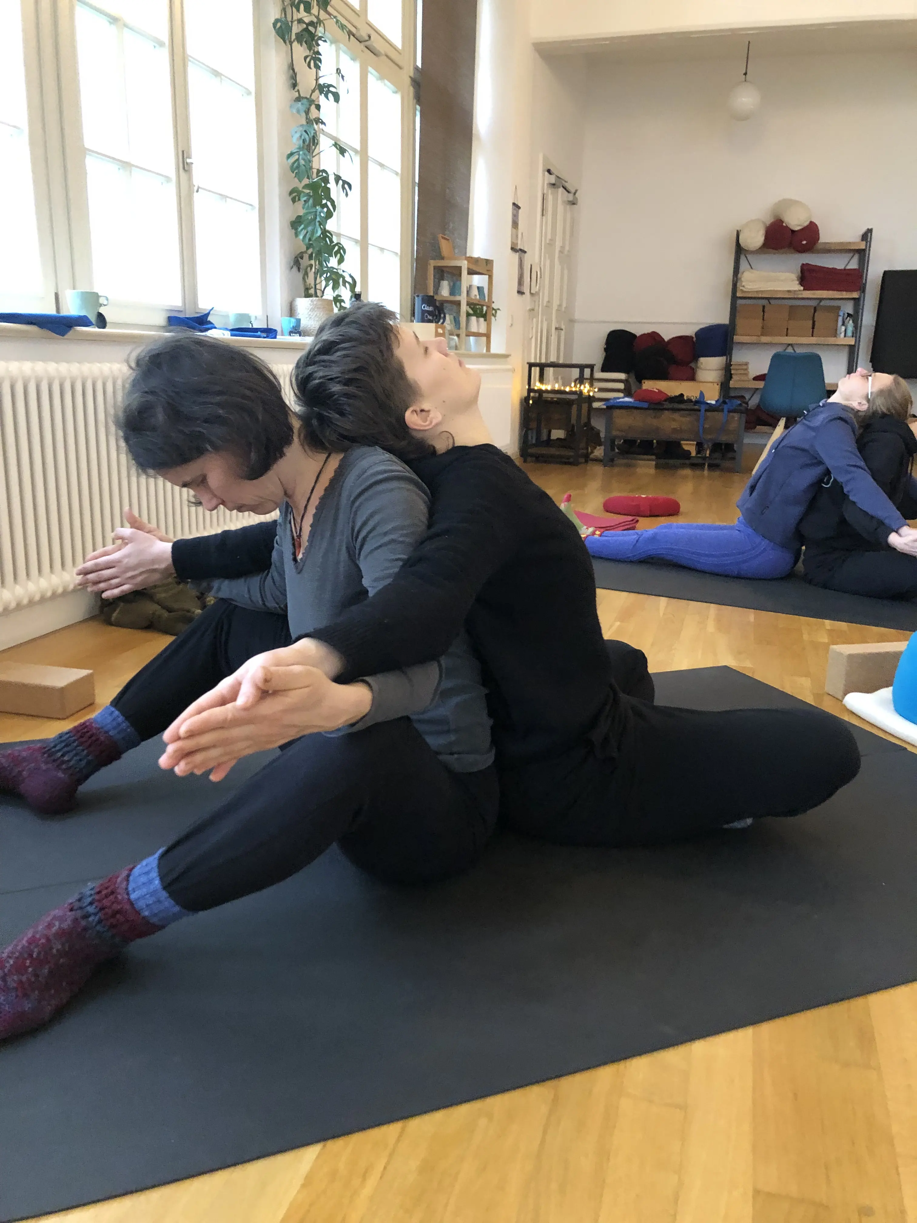 Teilnehmende in einer Partner-Yoga-Pose im Studio mit sichtbarer Raumstimmung